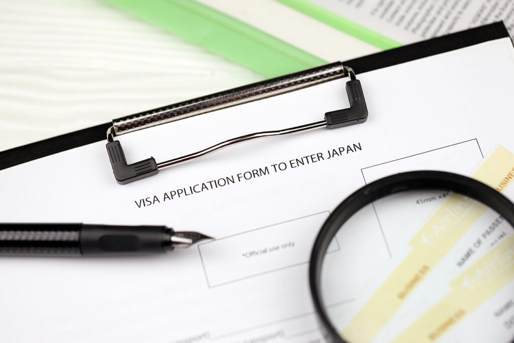 Visa application to enter Japan on A4 tablet lies on office table with pen and magnifying glass close up